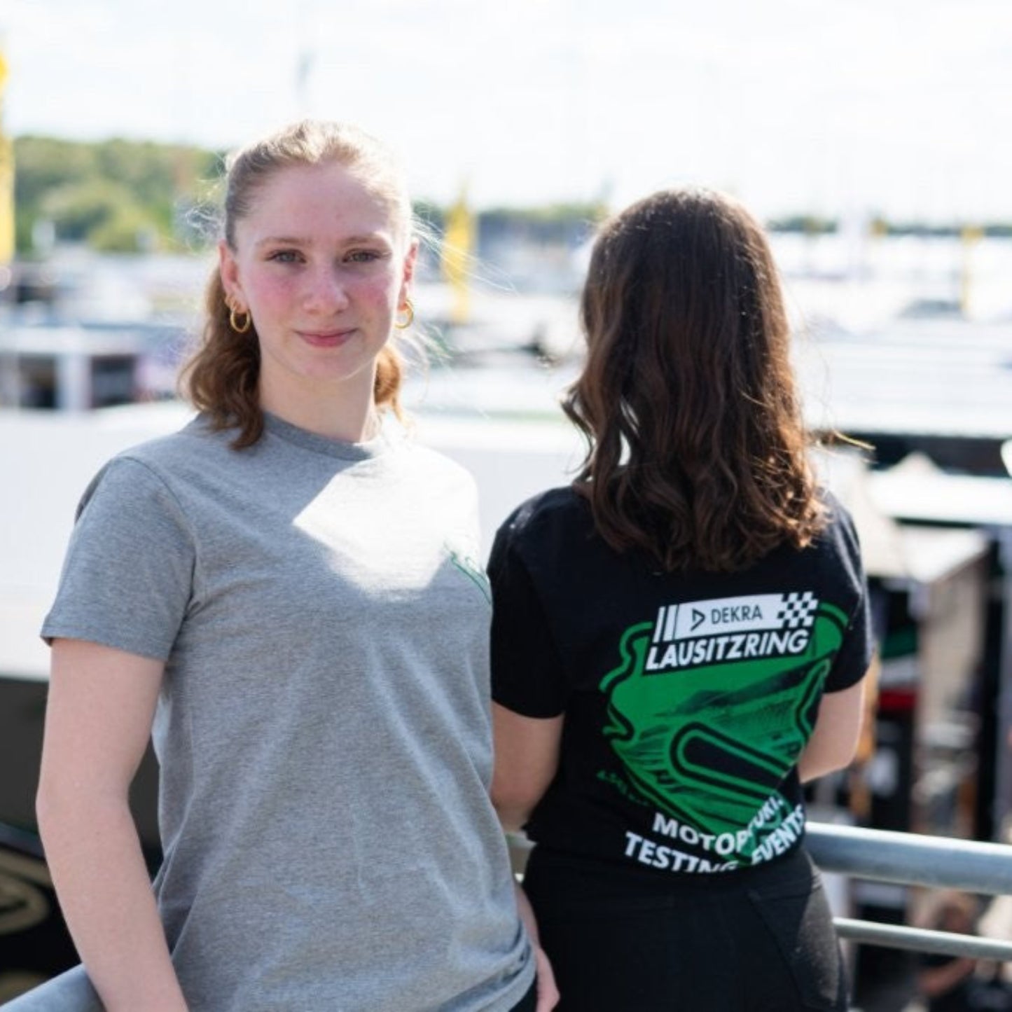 Zwei Personen tragen das T-Shirt Motorsport, Testing & Events mit DEKRA Lausitzring Logo, Vorder- und Rückansicht des sportlichen Teamshirts für Motorsportfans und Teilnehmer