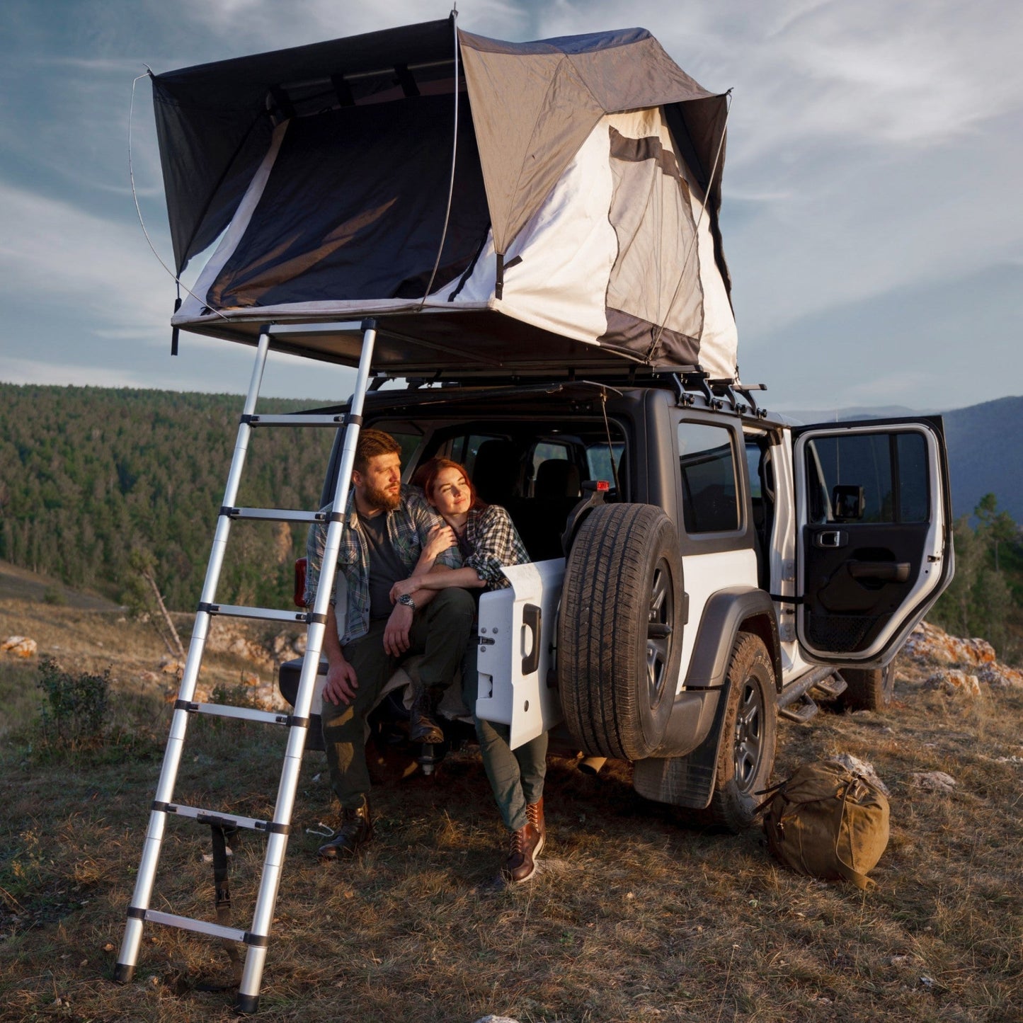 Ein Paar sitzt entspannt am Geländewagen mit aufgebautem Dachzelt inmitten einer natürlichen Landschaft, Symbolfoto für das Dachzelt- und Allradcamp am DEKRA Lausitzring.