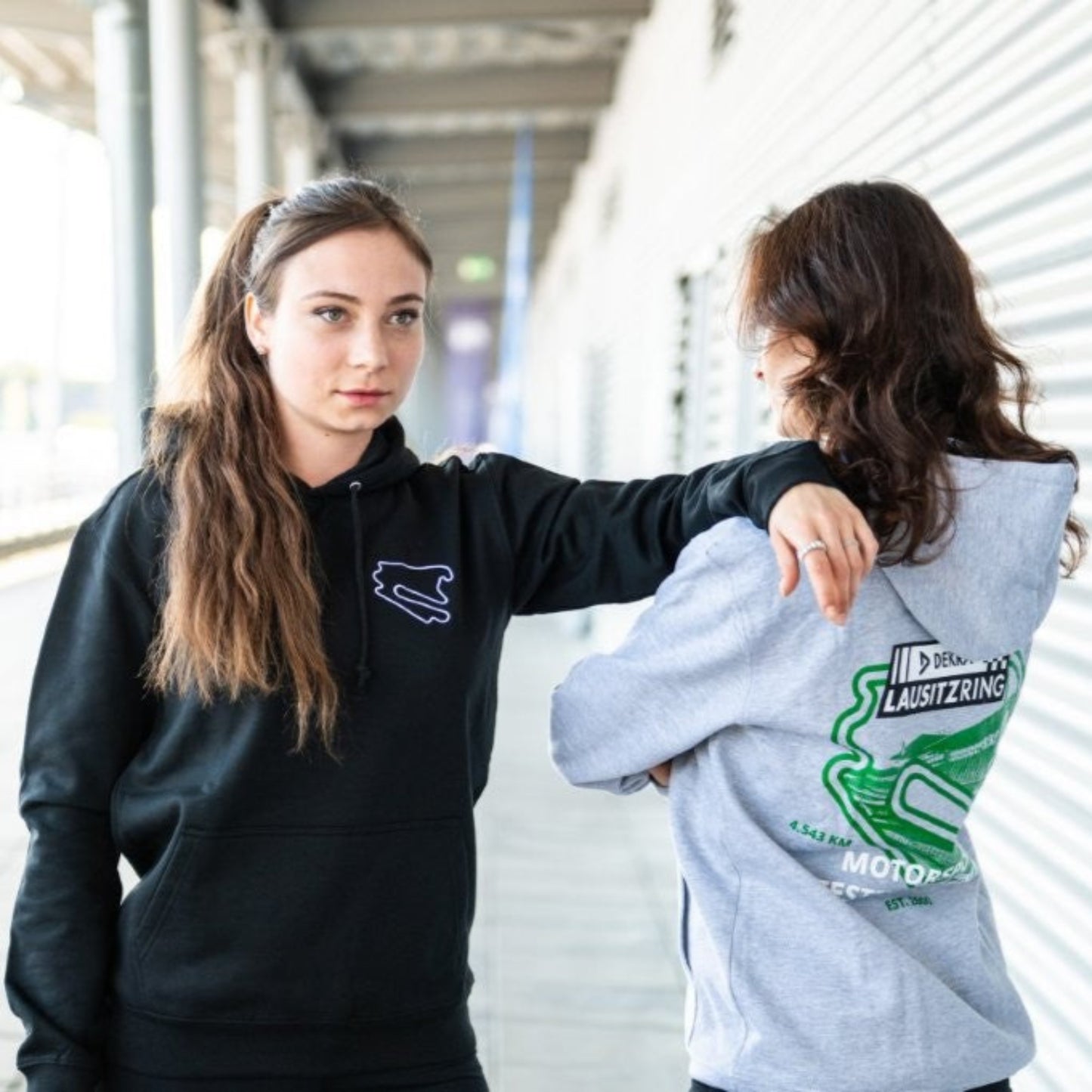 Zwei Personen tragen den Hoodie Motorsport, Testing & Events am DEKRA Lausitzring, sportliche Teamwear mit Strecken-Logo in Schwarz und Grau für Motorsportfans