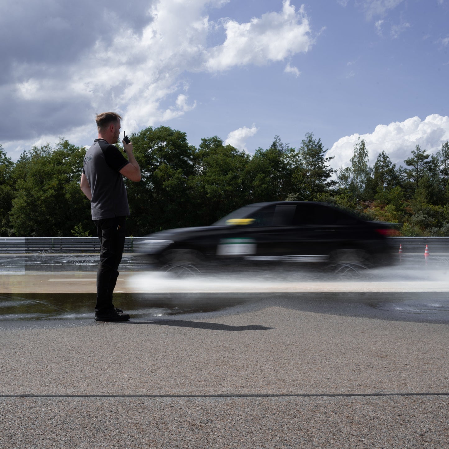 Trainer beobachtet Fahrzeug beim PKW Basis-Training am DEKRA Lausitzring, praxisorientiertes Fahrsicherheitstraining mit Brems- und Ausweichübungen auf nasser Fahrbahn