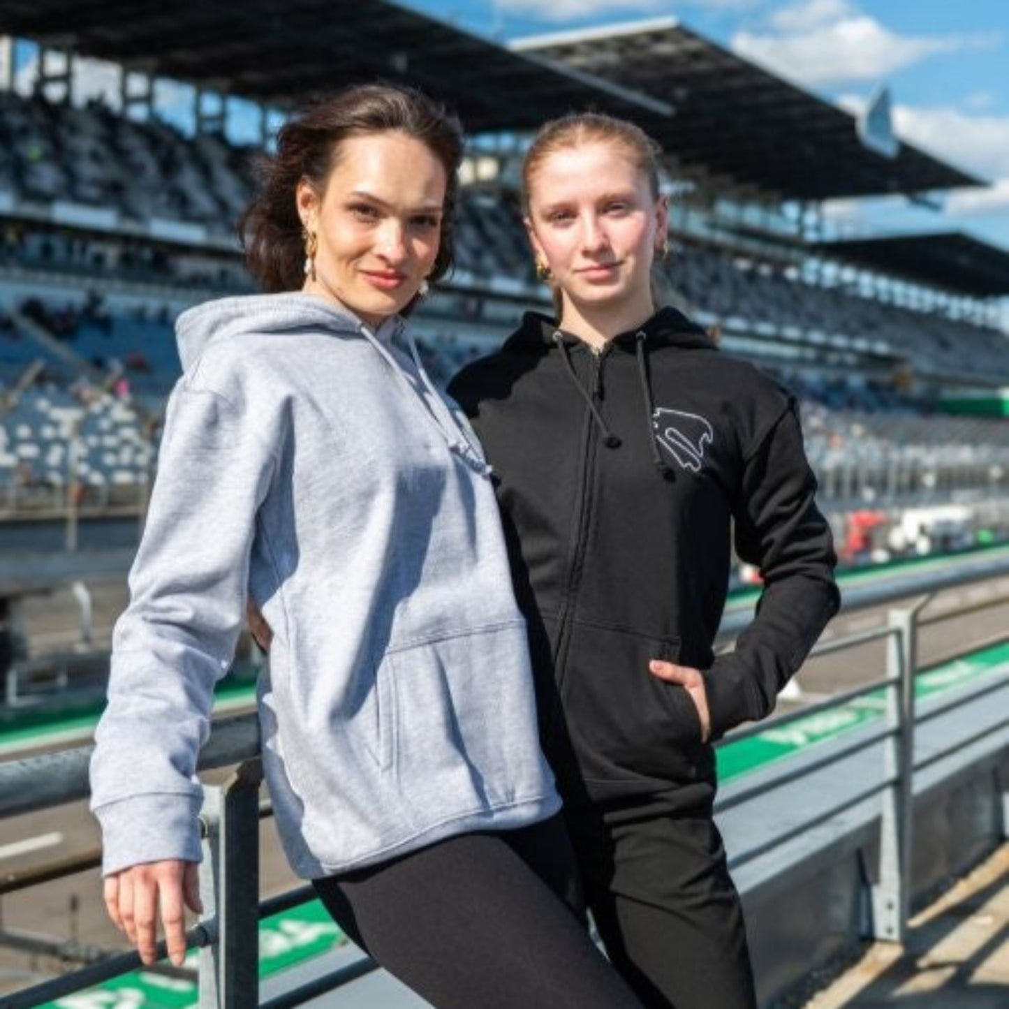 Zwei Personen tragen den Zip Hoodie Motorsport, Testing & Events auf der Tribüne des DEKRA Lausitzrings, sportliche und bequeme Teamwear für Motorsportfans und Teilnehmer